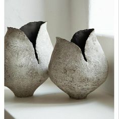 two gray vases sitting on top of a white table next to each other in front of a window