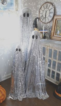 two silver ghost statues sitting on top of a wooden table next to a clock and window