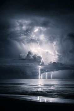 a black and white photo of lightning striking over the ocean