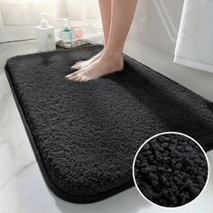 a person standing on top of a black rug in a bathroom next to a bathtub