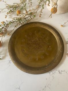 a gold plate sitting on top of a white counter next to flowers and vases