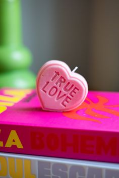 a heart shaped lollipop sitting on top of a pink book with the words true love written on it