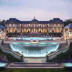 a large mansion with a fountain in front of it at night time and lit up by lights