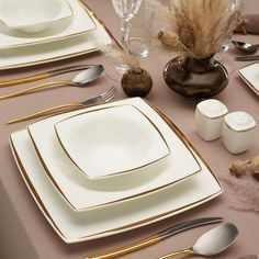 the table is set with white and gold plates, silverware, and vases