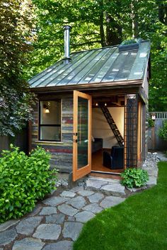 a small wooden shed with a metal roof and stairs leading up to the outside door