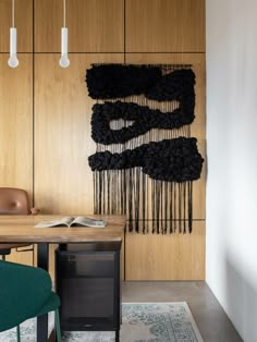 a room with a table, chair and art work on the wall above it that is covered in black yarn