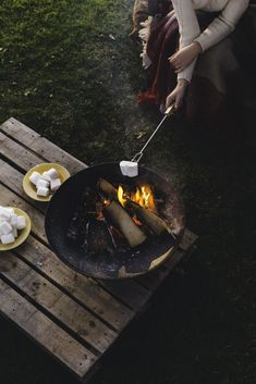 a woman is cooking marshmallows over an open fire on a picnic table