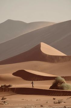 a person standing in the middle of a desert with sand dunes and mountains behind them