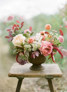 a vase filled with lots of flowers sitting on top of a wooden table in the grass