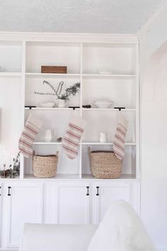 a living room filled with white furniture and baskets on top of the bookshelves