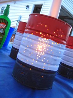 several buckets with lights on them sitting on a blue tarp covered table in front of a house