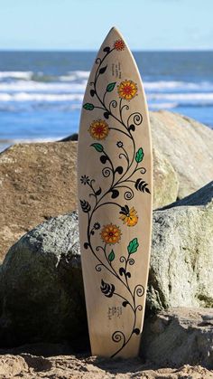 a wooden surfboard sitting on top of a sandy beach next to the ocean with flowers painted on it