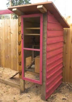 a pink outhouse in the middle of a fenced off area with a window