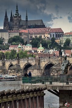 a bridge that has a statue on it in front of some buildings and a river