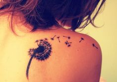 a woman's back shoulder with a dandelion tattoo