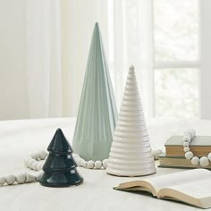 three ceramic trees are sitting on a table next to an open book and some beads