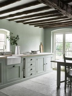 a kitchen with green cabinets and white counter tops next to a dining room table in front of two windows