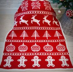 a crocheted blanket with reindeers and snowflakes on it next to a christmas tree