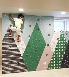 a young boy climbing up the side of a wall covered in colorful paper trees and polka dots