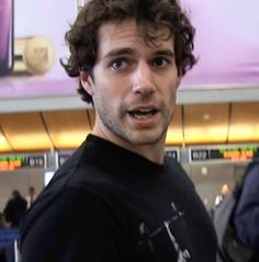 a man with curly hair standing in an airport