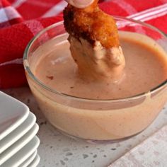 a person dipping something into a glass bowl filled with sauce on top of a red and white checkered table cloth