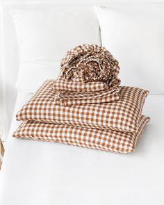 a bed with white sheets and brown checkered blankets on top of it, sitting next to pillows