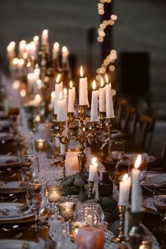 the table is set with many candles and plates on it, along with other place settings