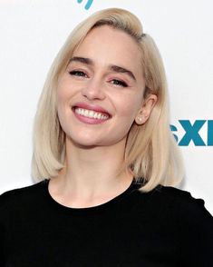 a woman with blonde hair smiling and wearing a black t - shirt at an event