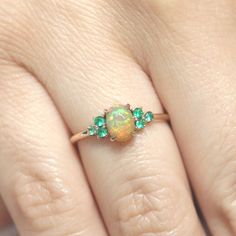 a woman's hand with an opal and emerald ring on top of her finger