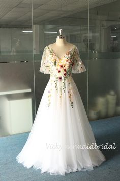 a white dress with flowers on it in front of a glass display case at a museum