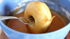 an apple being eaten with a fork in a blue bowl filled with liquid and sauce