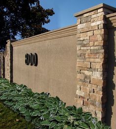 a sign that is on the side of a building with plants growing in front of it