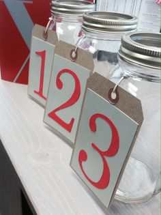 three mason jars with tags on them are sitting on a white counter top, one is empty and the other has red numbers