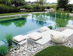 a large pool surrounded by rocks and grass with two white pillows on the end, sitting next to it