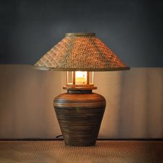 a table lamp sitting on top of a wooden floor next to a wall with a woven shade over it