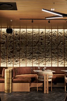 a restaurant with wooden tables and brown leather couches in front of a stone wall