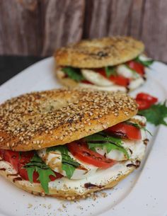 two bagel sandwiches with tomatoes, cheese and lettuce on a white plate