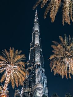 the burj tower is lit up at night with palm trees in front of it