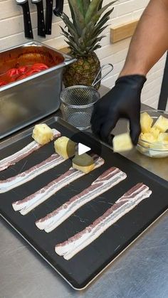 a person in black gloves cutting up food on a tray with pineapples and other foods