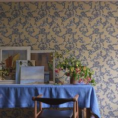 a blue table cloth on top of a wooden chair in front of a painting and flowers