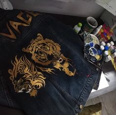 a pair of jeans with gold tiger designs on them and some paintbrushes next to it