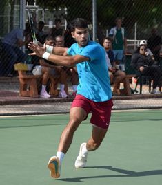 a man swinging a tennis racquet at a ball on a court with people watching