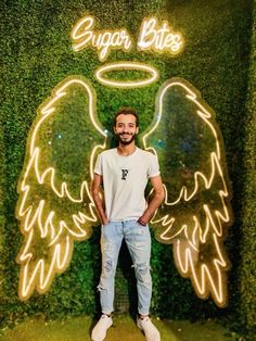 a man standing in front of a green wall with angel wings on it's side