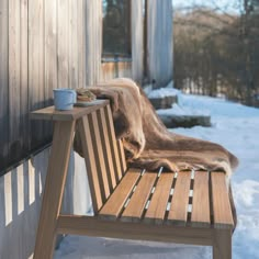 a wooden bench sitting next to a building with a cup on it's side