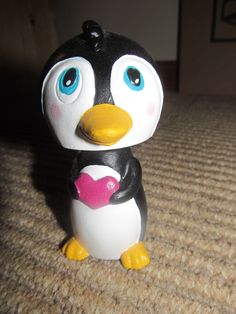 a small toy penguin with blue eyes and a pink heart on its chest sitting on the floor