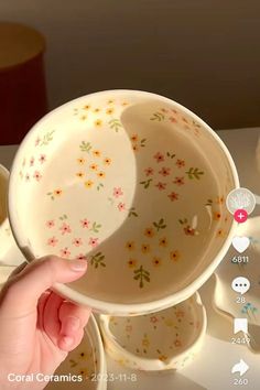 a person is holding a bowl in front of some cups and saucers on a table