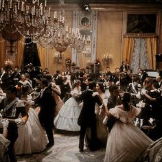 a group of people dressed in formal clothing dancing together with chandeliers hanging from the ceiling