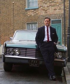 a man in a suit leaning on the hood of a car