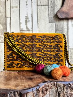 a yellow and black purse sitting on top of a wooden table next to balls of yarn