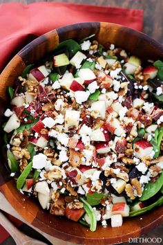 a wooden bowl filled with spinach, apples and feta cheese on top of a red napkin